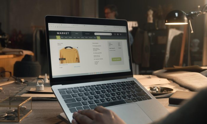 African American client in luxury designer atelier browsing online shop on laptop, watching clothing range, chooses sweatshirts. Concept of fashion and internet shopping. Close up view.